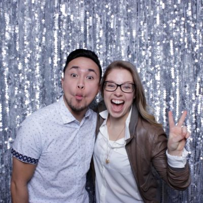 A woman with her hand in a peace sign and a man making a funny face in front of a glittery backdrop